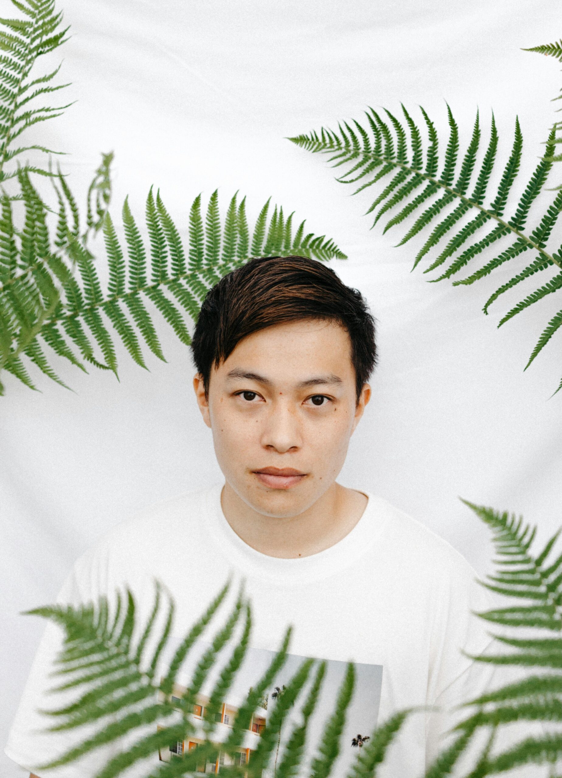 Asian man in white t-shirt with fern leaves against a white background.